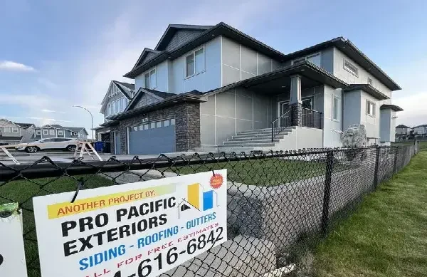 Grey panel siding and stone accents on a two-storey home behind a Pro Pacific project sign
