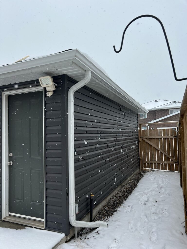 Hail punctures in dark horizontal vinyl siding beside a white downspout