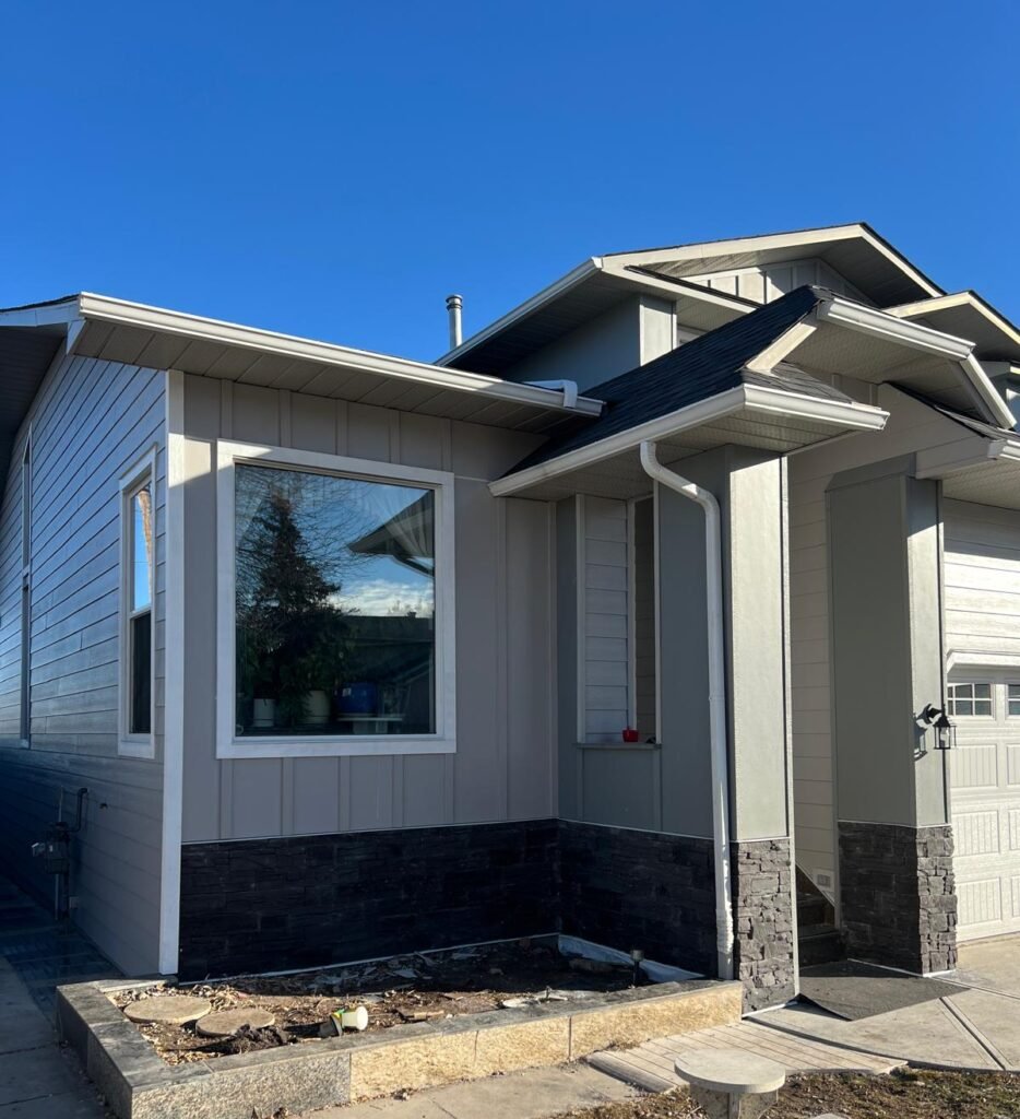 Light grey panel and lap siding with white trim and a dark stone base