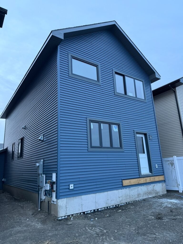 Rear and side of two-storey Alpine Park Calgary new-build home finished with blue horizontal vinyl siding and matching trim.