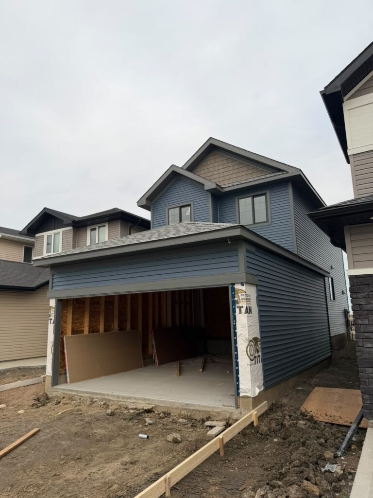 Exterior Contractor Calgary | Siding & Roofing | Pro Pacific Front of Alpine Park SE Calgary new-build home with completed blue vinyl siding, charcoal trim and attached garage.