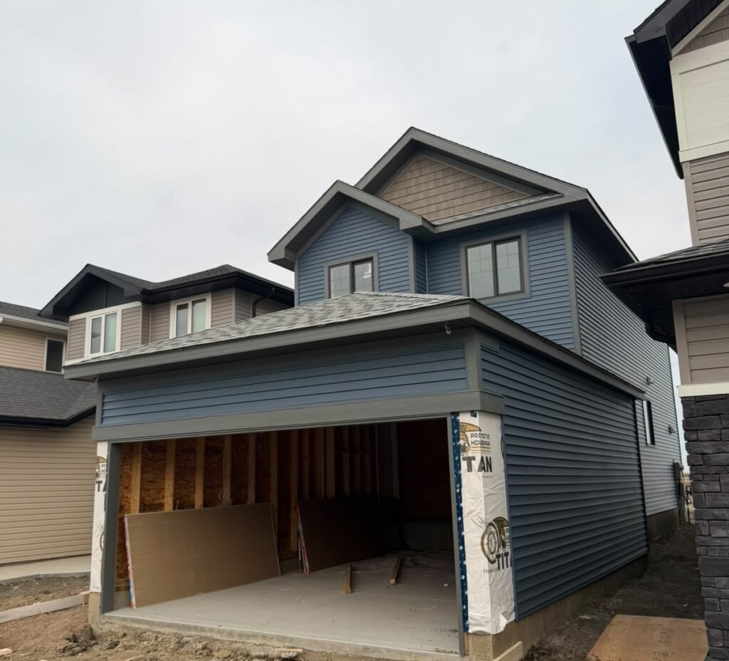 Front of Alpine Park SE Calgary new-build home with completed blue vinyl siding, charcoal trim and attached garage.